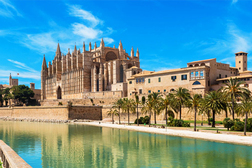 De kathedraal van Palma Mallorca met een groene waterpartij ervoor en blauwe lucht op de achtergrond
